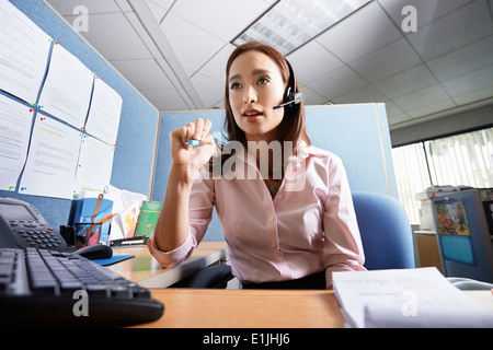 Junge weibliche Büroangestellte am Kopfhörer im Büro sprechen Stockfoto