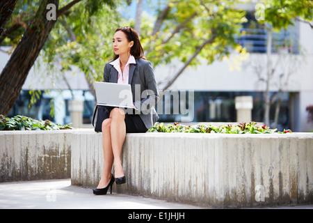 Junge weibliche Unternehmerin mit Laptop vor Büro Stockfoto
