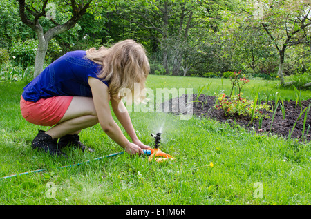 Mädchen dreht auf die Gartenbewässerung an den jungen Blume Sämling Stockfoto