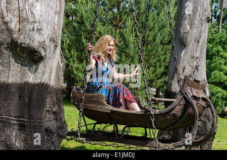 Junge, blonde Frau in antiken hölzernen Schlitten antike dekorative Schaukeln schwingen Stockfoto