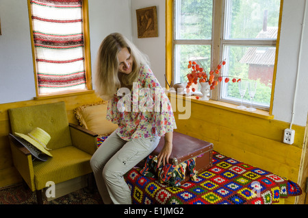 lächelnde junge Frau sitzen auf gepolsterten Koffer im ländlichen Bettzimmer Stockfoto