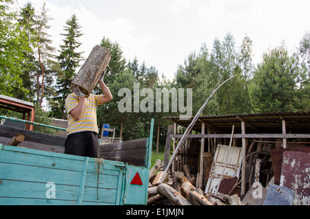 Arbeiter Mann entladen Baum protokolliert Brennholz Holz aus Traktoranhänger in der Nähe von ländlichen Holzschuppen Haus. Stockfoto