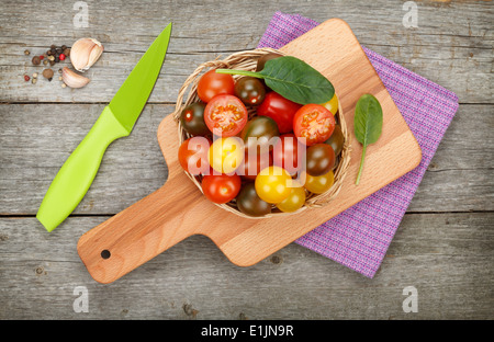 Bunte Kirschtomaten mit Gewürzen und Messer auf Schneidebrett über Holztisch Hintergrund Stockfoto