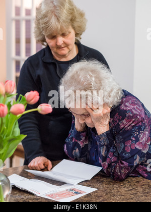 Liest einen Brief. Eine ältere Frau liest einen Brief mit dem Kopf in ihren Händen, während ihre Tochter schaut. Stockfoto