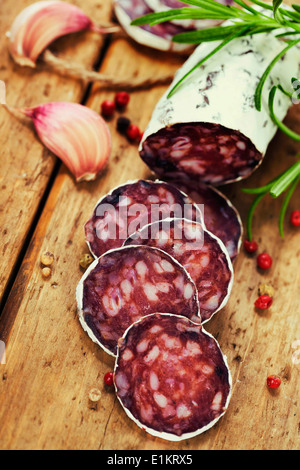 Close-up traditionell geschnittene Fleisch Wurst Salami auf Holzbrett mit Kopf von Knoblauch und grünen Kräutern Stockfoto