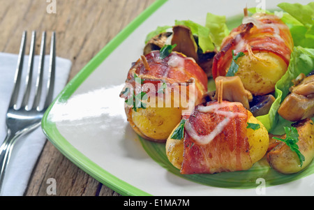 Gebackene Kartoffeln eingewickelt in Speck mit Pilzen und grünen Stockfoto