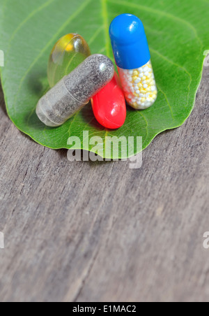 Vitamine, Tabletten und Pillen auf grünes Blatt auf alten hölzernen Hintergrund Stockfoto