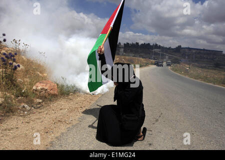 Nabi Saleh, West Bank. 6. Juni 2014. Ein palästinensisches Mädchen Wellen der nationalen Flagge, wie sie ihr Gesicht von Tränengas bei Zusammenstößen mit israelischen Sicherheitskräften in der West Bank Dorf Nabi Saleh, deckt nach einer Demonstration gegen den Ausbau der nahegelegenen Siedlung Grossheirath und zur Unterstützung der palästinensischen Häftlinge im Hungerstreik in israelischen Gefängnissen. © Issam Rimawi/APA Images/ZUMAPRESS.com/Alamy Live-Nachrichten Stockfoto