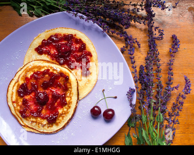 Leckere Pfannkuchen auf einem Tisch, umgeben von lila Blüten Stockfoto