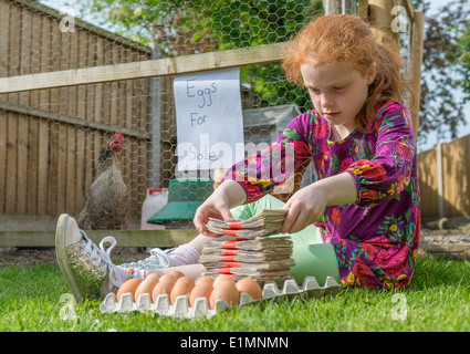Kleine Mädchen Unternehmer sitzt mit Tausende von Pfund, während Hennen Eiern verkaufen. Stockfoto