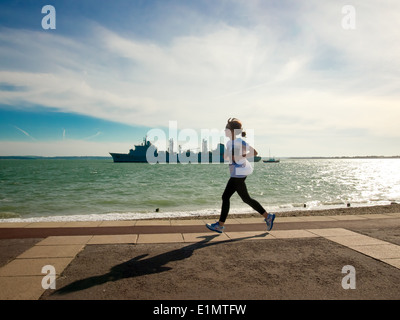 Eine junge Frau läuft entlang Southsea Seafront als FS Somme Portsmouth Harbour verlässt. Stockfoto