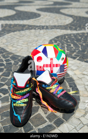 Viel Glück Fußballschuhe Stollen geschnürt mit brasilianischen Wunsch Bändern auf dem Copacabana Strand Gehweg mit internationalen Flagge ball Stockfoto