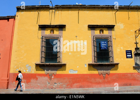 Gelbes und rotes Gebäude mit Fenstern und eine Person, die die Straße entlang geht, San Miguel de Allende, Guanajuato, Mexiko Stockfoto