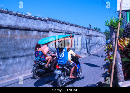 Touristen auf Fahrräder oder Roller mit Surfen Surfbretter auf dem Kopf in Richtung Strand in Kuta, Bali, Indonesien Stockfoto