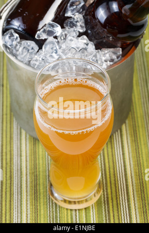 Closeup vertikale Foto von Longdrinkglas gefüllt mit goldener Farbe Bier mit Flaschenbier im Eiskübel im Hintergrund Stockfoto