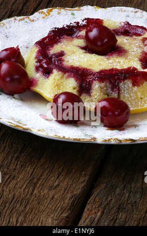 Vanille-Kuchen mit Sauerkirschen Puderzucker auf antike Teller groben dunklen hölzernen Hintergrund Stockfoto