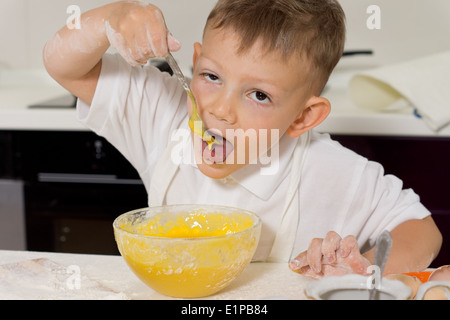 Junge, einen Vorgeschmack auf den Kuchenteig, da er in der Küche lernen steht, wie man seine Lieblings-Kuchen machen Stockfoto