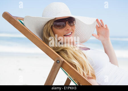 Wunderschöne Blondine sitzt am Strand tragen, Sonnenhut und Sonnenbrille Stockfoto
