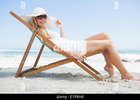 Wunderschöne Blondine sitzt am Strand tragen, Sonnenhut und Sonnenbrille Stockfoto