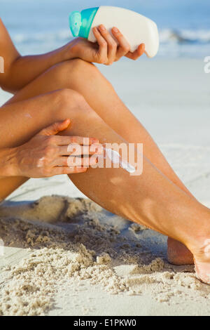 Frau sitzt am Strand Sonnencreme auftragen Stockfoto