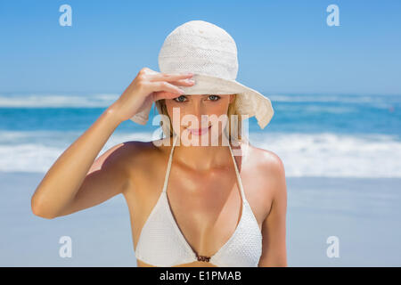 Lächelnde Blondine im weißen Bikini und Sonnenhut am Strand Stockfoto