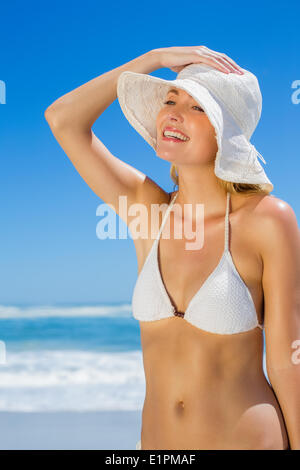 Lächelnde Blondine im weißen Bikini und Sonnenhut am Strand Stockfoto