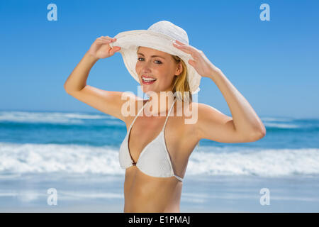 Lächelnde Blondine im weißen Bikini und Sonnenhut am Strand Stockfoto