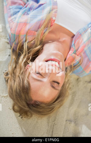 Hübsche Blondine lächelnd am Strand auf dem Sand liegen Stockfoto