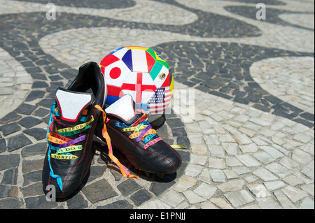 Viel Glück Fußballschuhe Stollen geschnürt mit brasilianischen Wunsch Bändern auf dem Copacabana Strand Gehweg mit internationalen Flagge ball Stockfoto