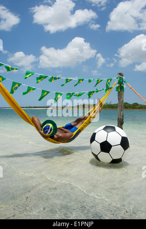 Brasilianischer Fußballspieler Entspannung in Strand-Hängematte mit einem schwebenden Fußball Stockfoto