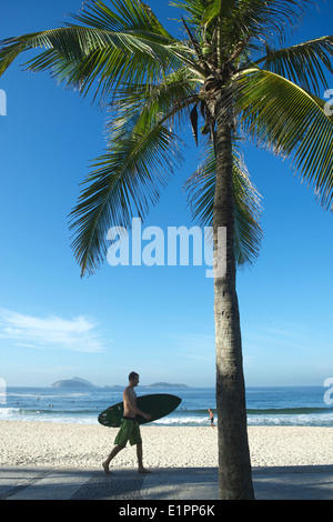 RIO DE JANEIRO, Brasilien - 21. Februar 2014: Mann trägt Surfbrett entlang der Promenade am Arpoador entlang einen Blick auf den Strand von Ipanema. Stockfoto