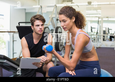 Trainer beobachten Client Aufzug Hanteln auf Gymnastikball Stockfoto