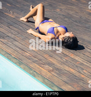 Schlanke Brünette im lila Bikini liegen am Pool Stockfoto