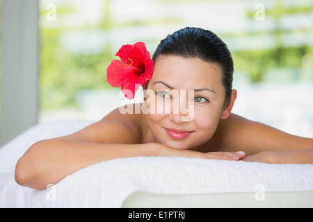 Lächelnde Brünette auf Massagetisch liegend mit rote Lilie im Haar Stockfoto