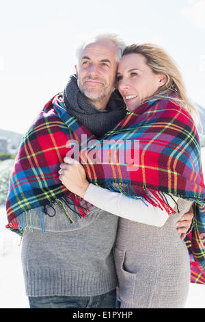 Glückliches Paar eingehüllt in Decke stehen am Strand Stockfoto
