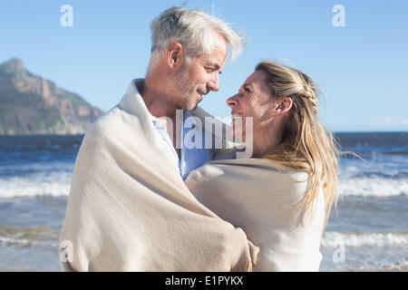 Lächelnde paar eingehüllt in Decke am Strand Stockfoto