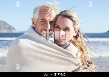 Lächelnde paar eingehüllt in Decke am Strand Stockfoto