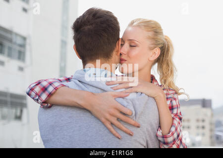 Hüft-junges Paar umarmt mit Frau, die ihn auf die Wange küssen Stockfoto