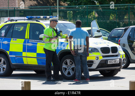 Polizist im Gespräch mit schwarzer Mann von Polizei-Auto. Stockfoto