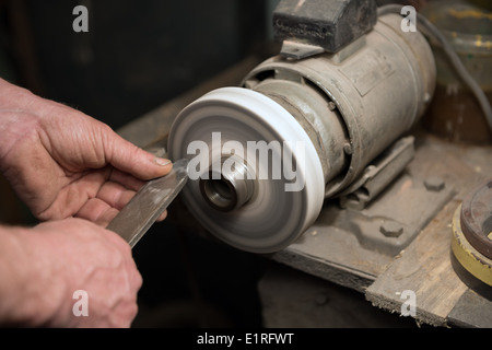 Hände des Handwerkers halten Stemmeisen hausgemachte Drehmaschine während des Schärfens auf hausgemachte Schleifmaschine. Stockfoto