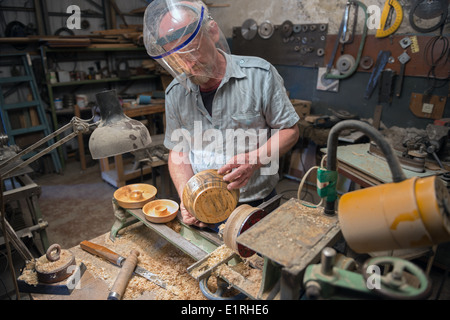 Gealterte Mann prüft die hölzerne Ware nach dem Schleifen heraus auf Drehbank. Stockfoto