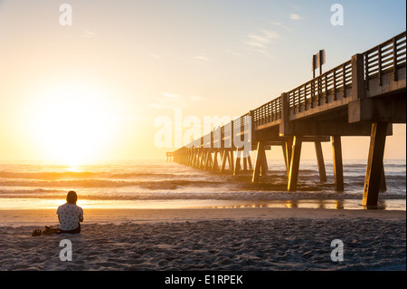 Junge Frau im Hintergrund eintauchen in die Schönheit und Wunder von einem dramatischen Sonnenaufgang in Jacksonville Beach, Florida, USA. Stockfoto