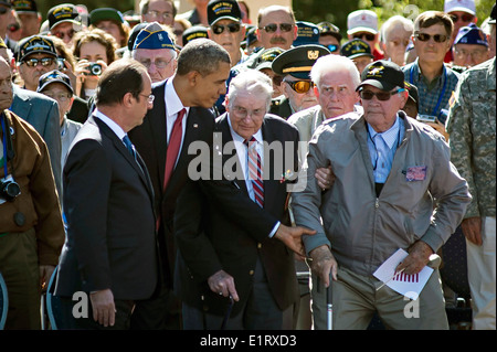 US-Präsident Barack Obama und der französische Präsident Francois Hollande hilft eine Veteran des zweiten Weltkriegs Normandie zurück in seinen Sitz anlässlich des 70. Jahrestages der d-Day in der Normandie amerikanischen Friedhof und Denkmal 6. Juni 2014 in der Normandie, Frankreich. Stockfoto