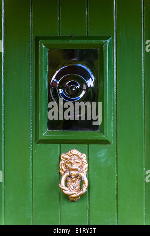 Türklopfer Messing mit Löwen Kopf, grünen Holztür und Bullen Auge Glas Fensterscheibe. Stockfoto