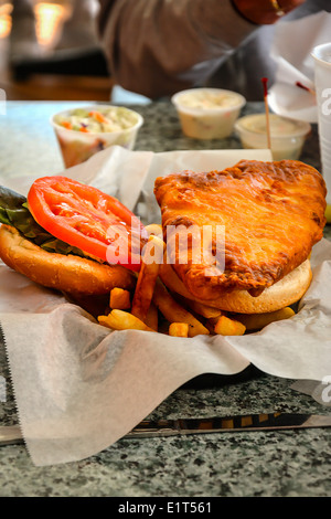 Tischplatte Nahaufnahme von einem A gebratenen Kabeljau Fisch-Sandwich mit Tomate, Pommes Frites mit Cole Slaw serviert in einem Korb Stockfoto