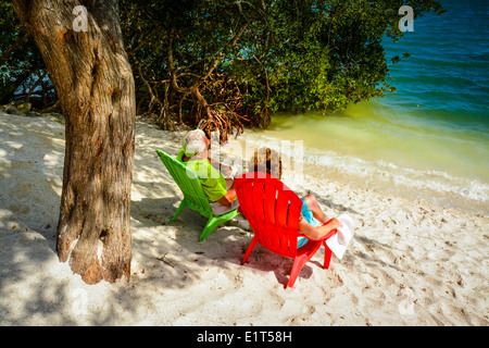 Anonyme älteres Paar genießen die Aussicht von ihrer bunten Strandkörbe in der Nähe von Wasser auf einem weißen Sandstrand Stockfoto