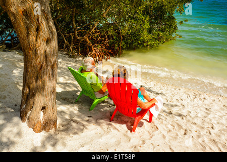 Anonyme älteres Paar genießen die Aussicht von ihrer bunten Strandkörbe in der Nähe von Wasser auf einem weißen Sandstrand Stockfoto