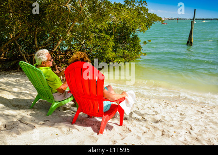 Anonyme älteres Paar genießen die Aussicht von ihrer bunten Strandkörbe in der Nähe von Wasser auf einem weißen Sandstrand Stockfoto