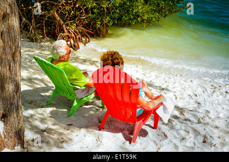 Anonyme älteres Paar genießen die Aussicht von ihrer bunten Strandkörbe in der Nähe von Wasser auf einem weißen Sandstrand Stockfoto