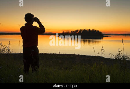 Mittleren Alters männlichen Wanderer Blick auf Astotin Lake mit dem Fernglas in der Abenddämmerung, Elk Island Park, Alberta, Kanada. Stockfoto